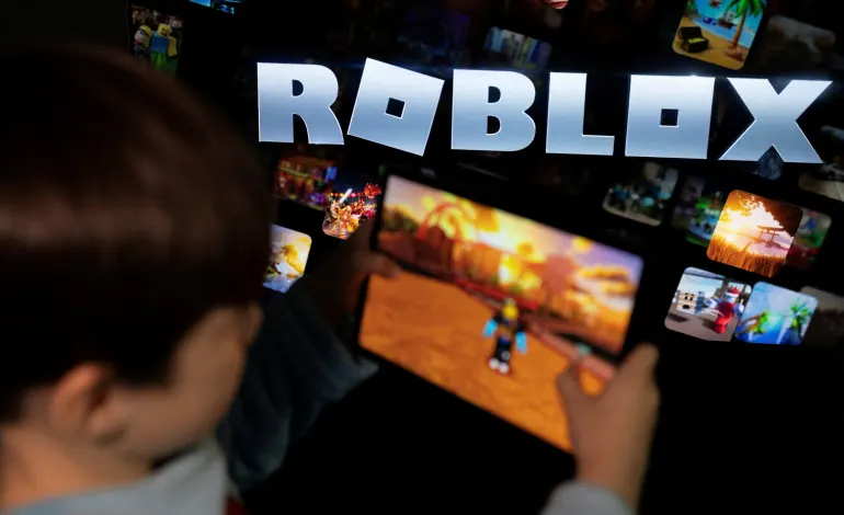 A boy poses for a photo while holding a game pad in front of a screen displaying the logo of the U.S. children's gaming platform Roblox, in this illustration taken December 8, 2025. Ramil Sitdikov/Illustration
