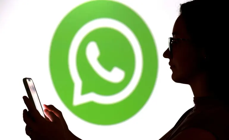 A teenager poses for a photo while holding a smartphone in front of a Whatsapp logo in this illustration taken September 11, 2025. Dado Ruvic/Illustration