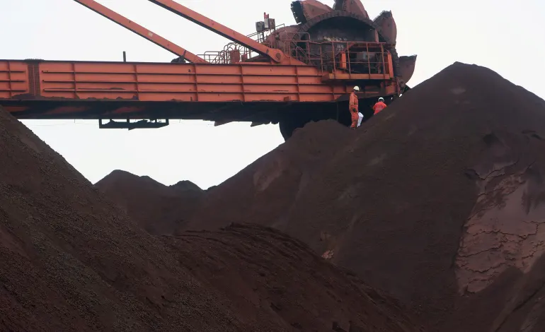 Workers are seen on the top of an iron ore pile as a machine works on blending the iron ore, at Dalian Port, Liaoning province, China September 21, 2018. Muyu Xu