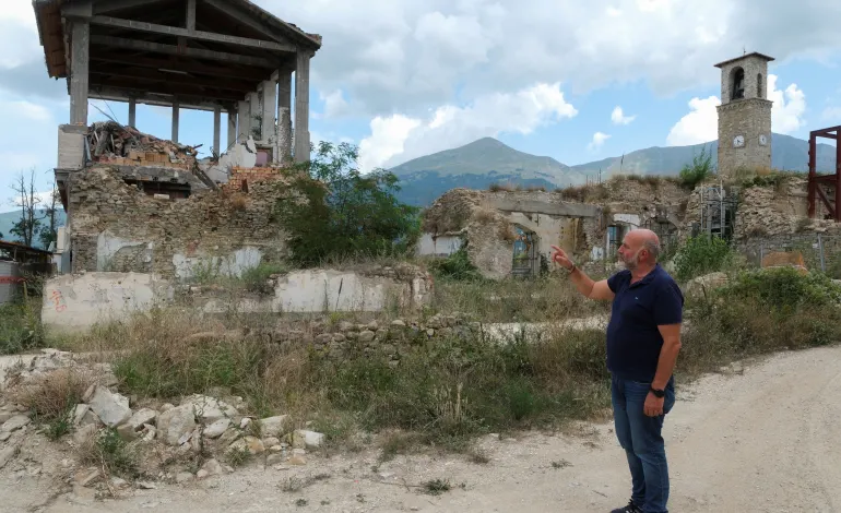 The Mayor of Amatrice, Giorgio Cortellesi, points to a destroyed building in the red zone ten years after an earthquake devastated Amatrice, central Italy, August 8, 2026. REUTERS/Crispian Balmer